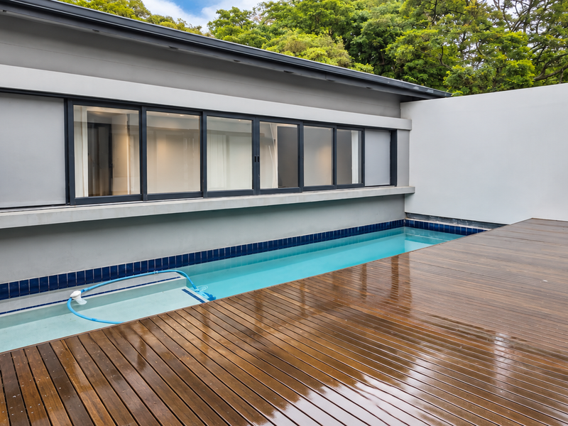 A modern outdoor pool area featuring a sleek swimming pool, timber decking, and large sliding glass doors providing seamless indoor-outdoor flow.