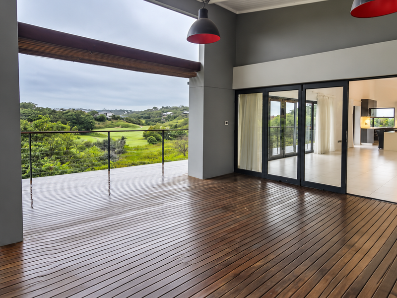 Spacious covered patio featuring timber decking, steel balustrades, and large sliding glass doors that open into the interior living area with scenic views.