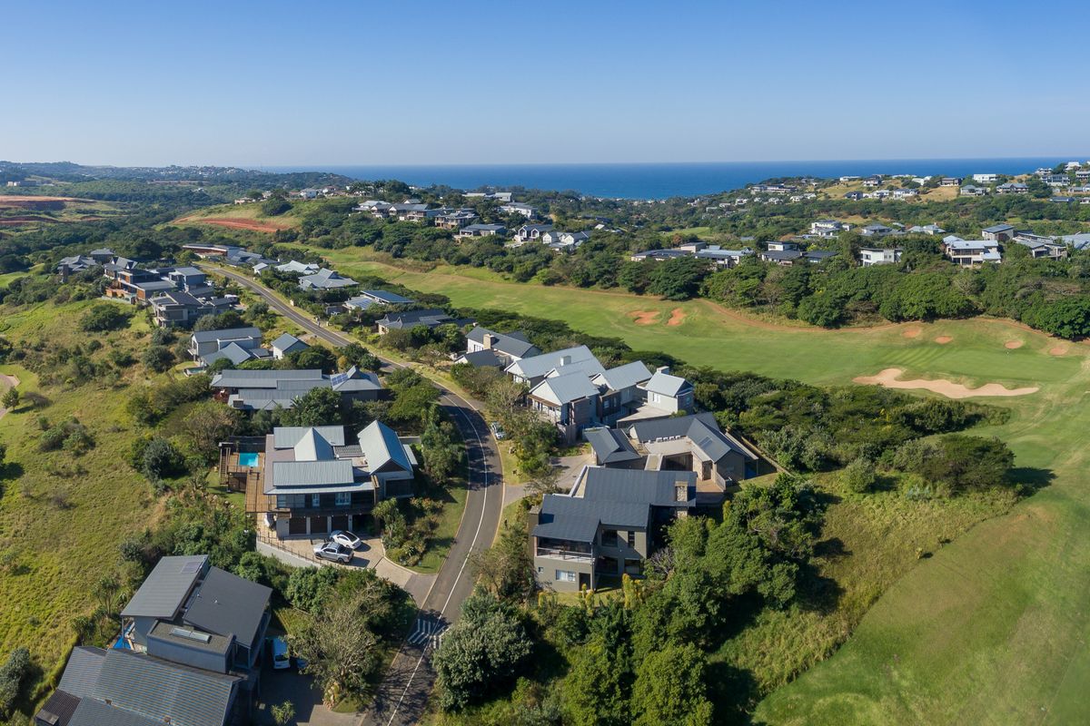 An expansive aerial view of a residential estate integrated into a golf course landscape with coastal views in the distance.