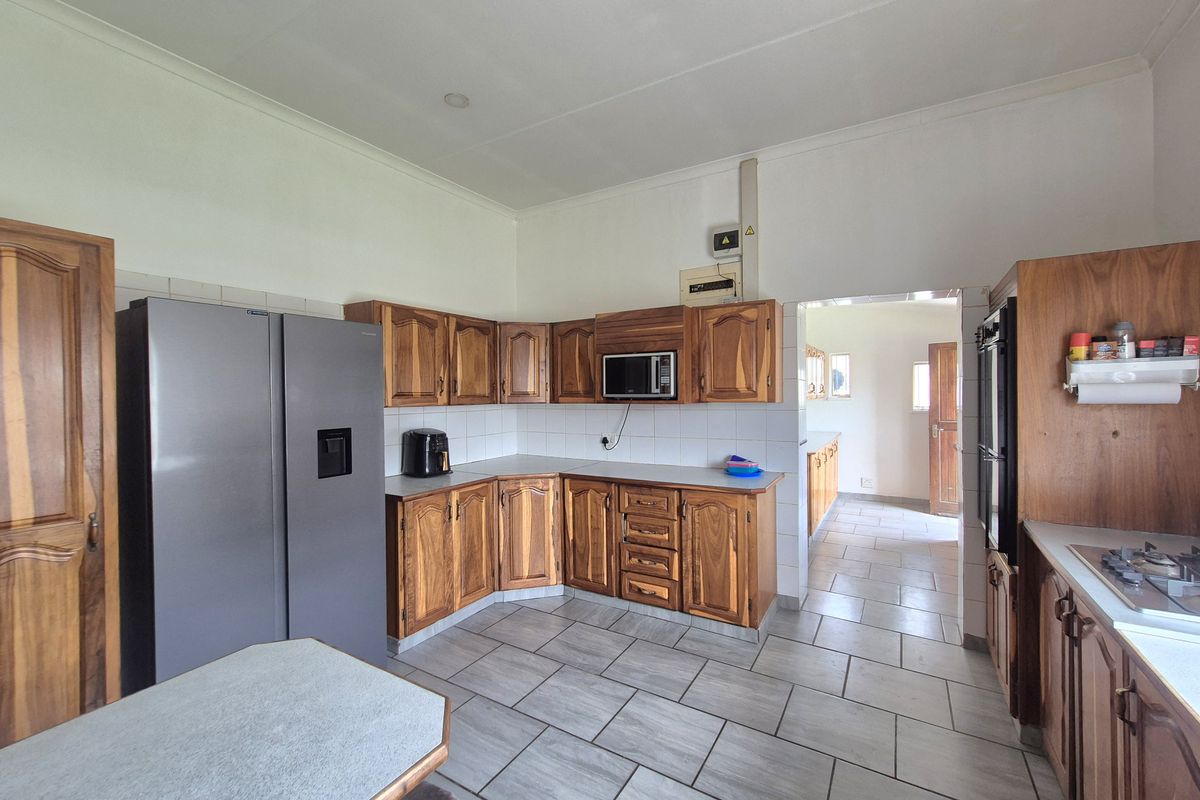 A functional kitchen featuring traditional wooden cabinetry, tiled flooring, and built-in appliances, with an adjacent scullery area visible through the doorway.