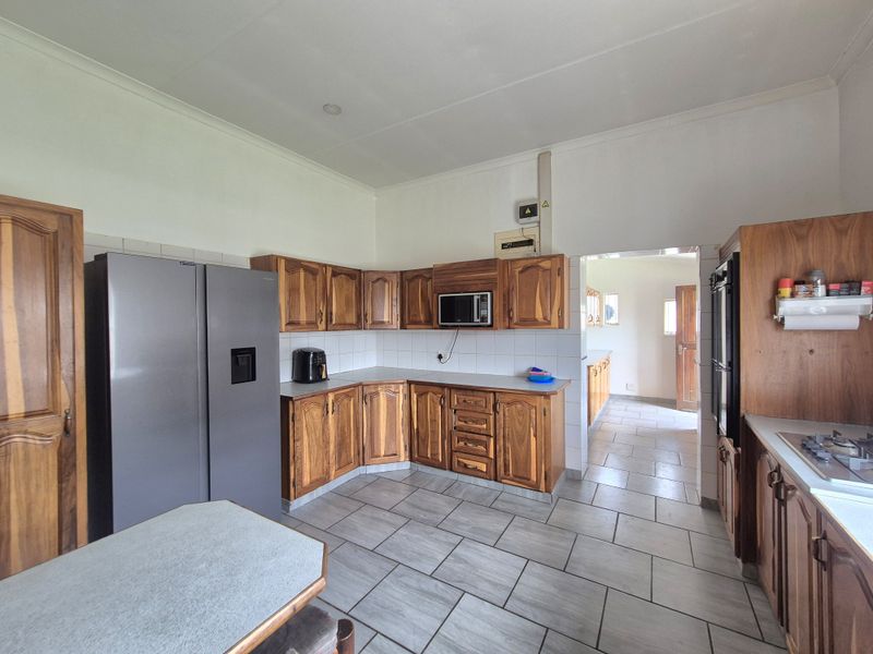 A functional kitchen featuring traditional wooden cabinetry, tiled flooring, and built-in appliances, with an adjacent scullery area visible through the doorway.