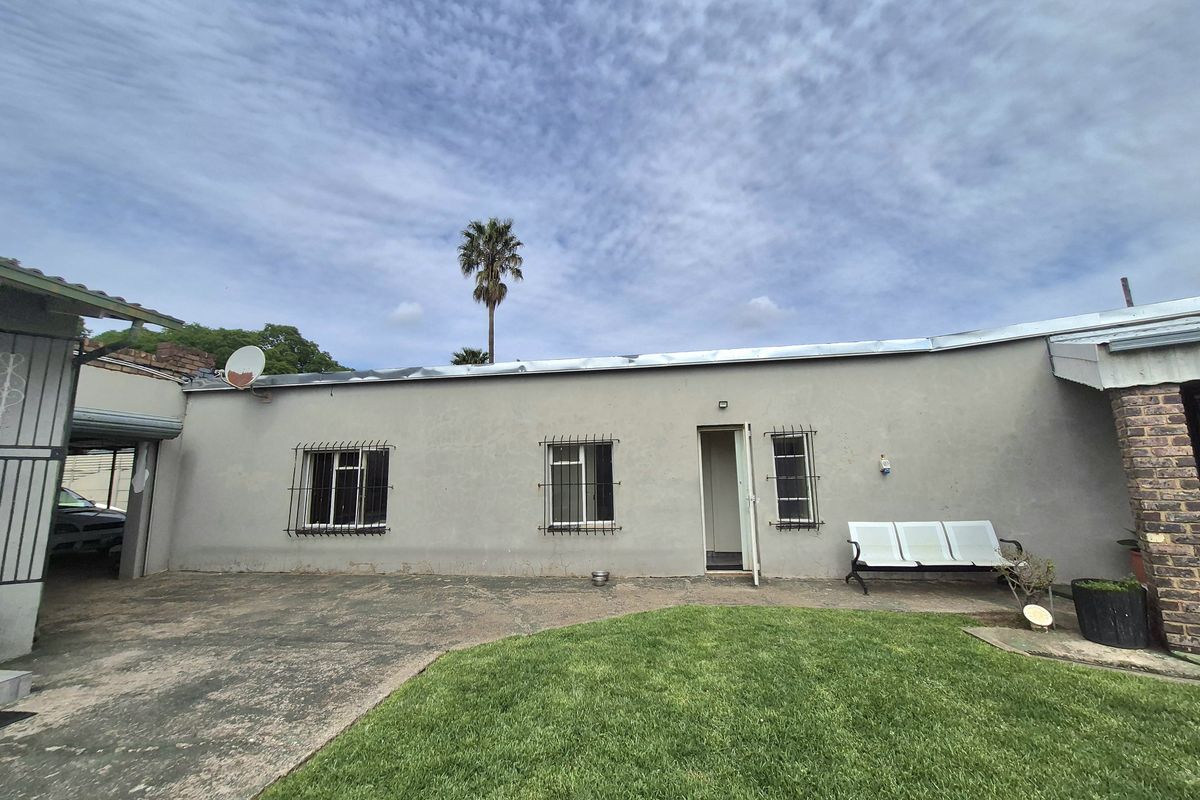 Rear exterior view of the house featuring a concrete patio area, lawn, and security bars on the windows.