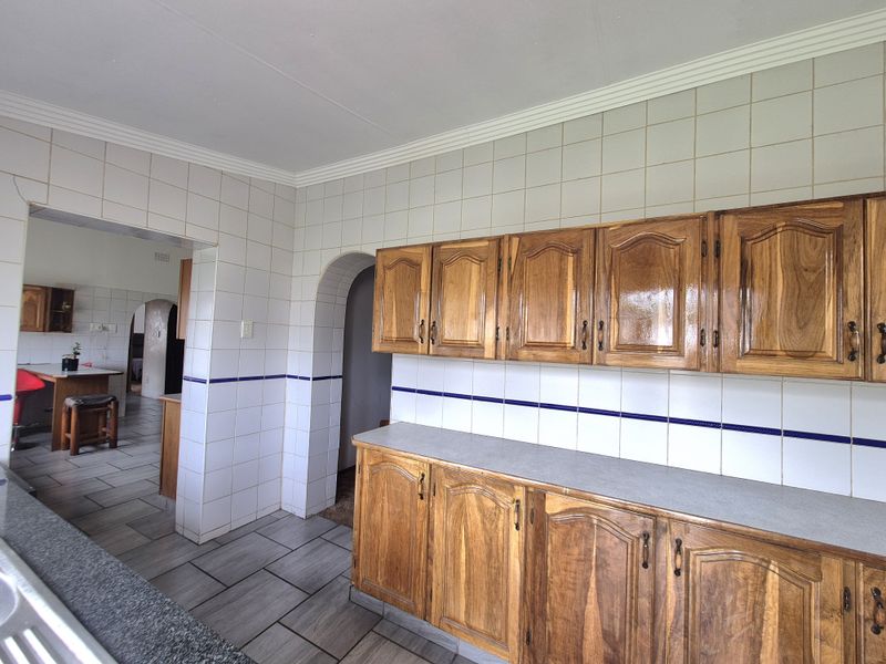 A dated kitchen featuring wooden cabinetry, tiled walls, and tiled flooring, with an open archway leading to an adjacent room.