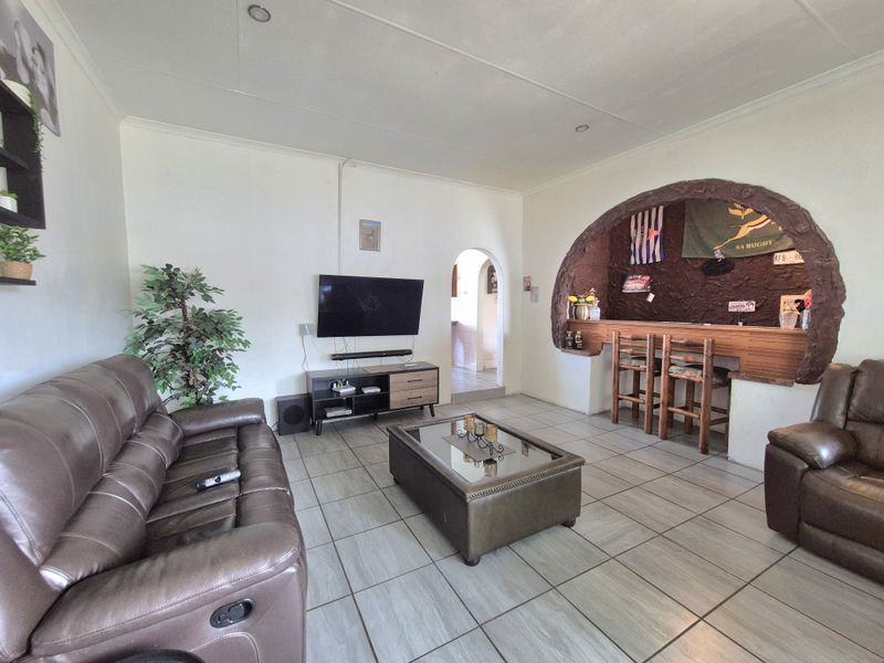 Spacious living room featuring tiled flooring, recessed lighting, and a unique built-in bar area set within a decorative stone-look archway.
