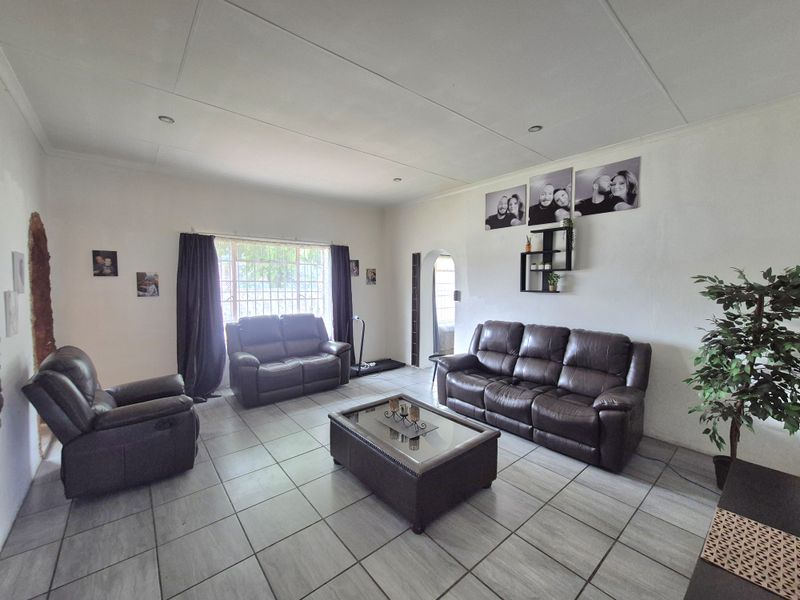 Spacious living room featuring neutral tiled flooring, large window with security bars, and a classic arched doorway leading to adjacent areas.