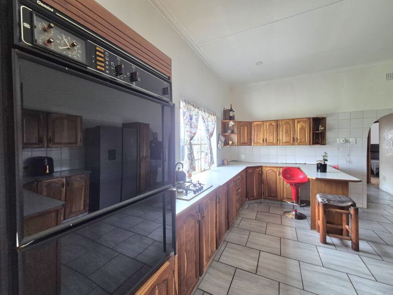 A functional kitchen featuring wooden cabinetry, a built-in eye-level oven, gas hob, tiled backsplash, and a breakfast counter area.