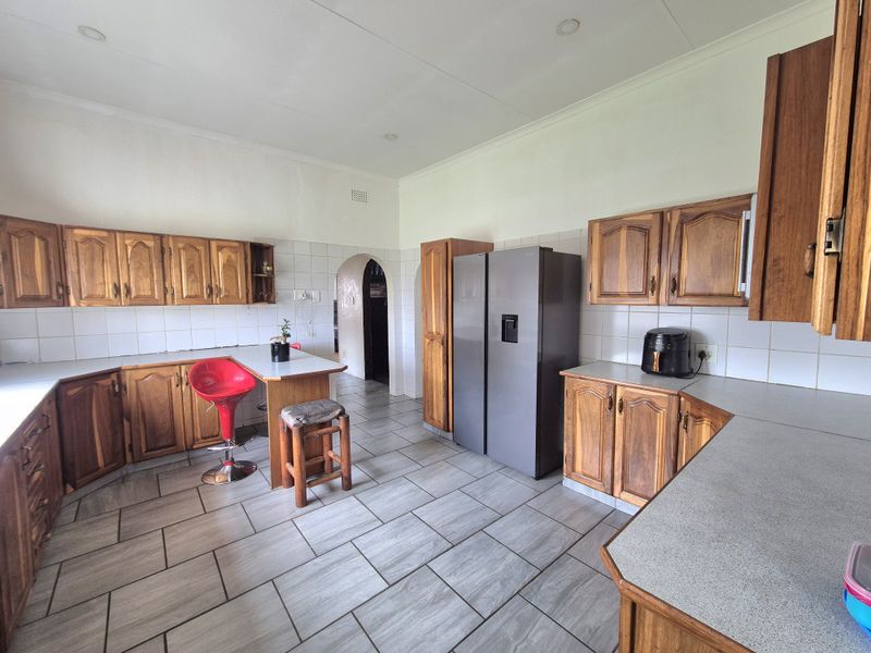 A functional kitchen featuring wooden cabinetry, tiled backsplash, and grey tiled flooring with a breakfast nook area and an arched doorway.
