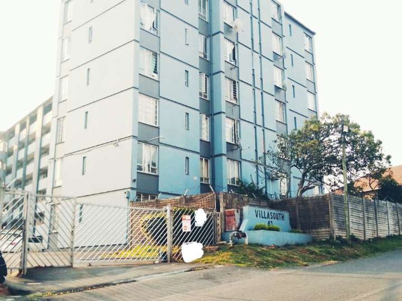 Exterior view of the Villasouth apartment complex, featuring a secure gated entrance, perimeter fencing, and multi-story residential building facade.