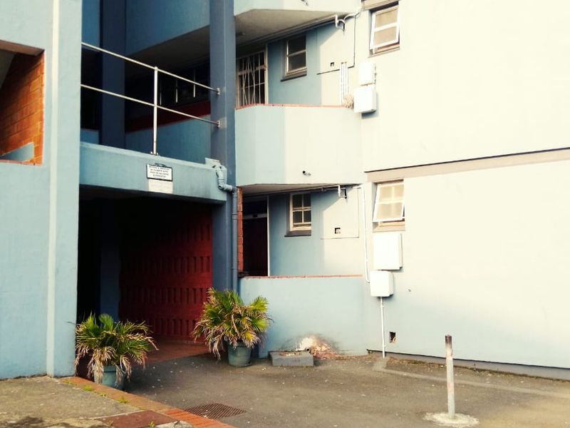 Exterior view of an apartment building facade featuring blue painted walls, brick accents, and multi-level balcony access points.