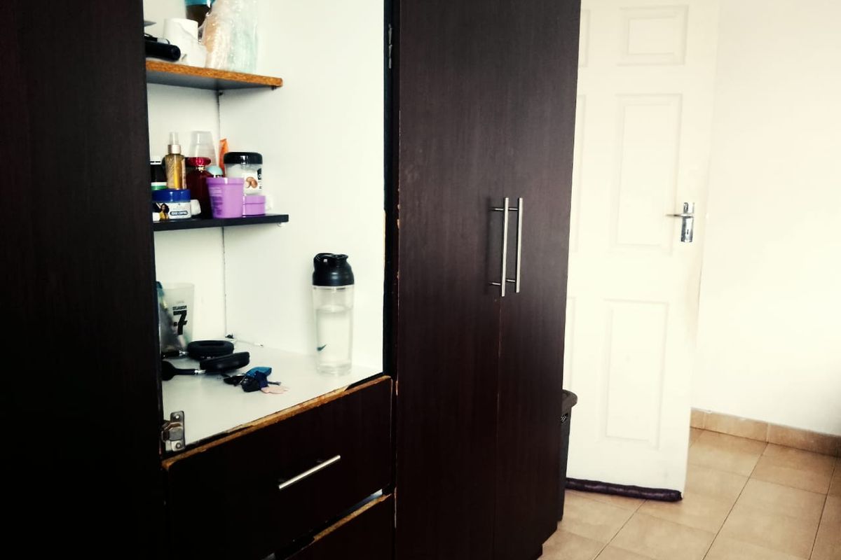 A bedroom featuring a dark wood built-in wardrobe with visible wear and tiled flooring, leading to an internal door.