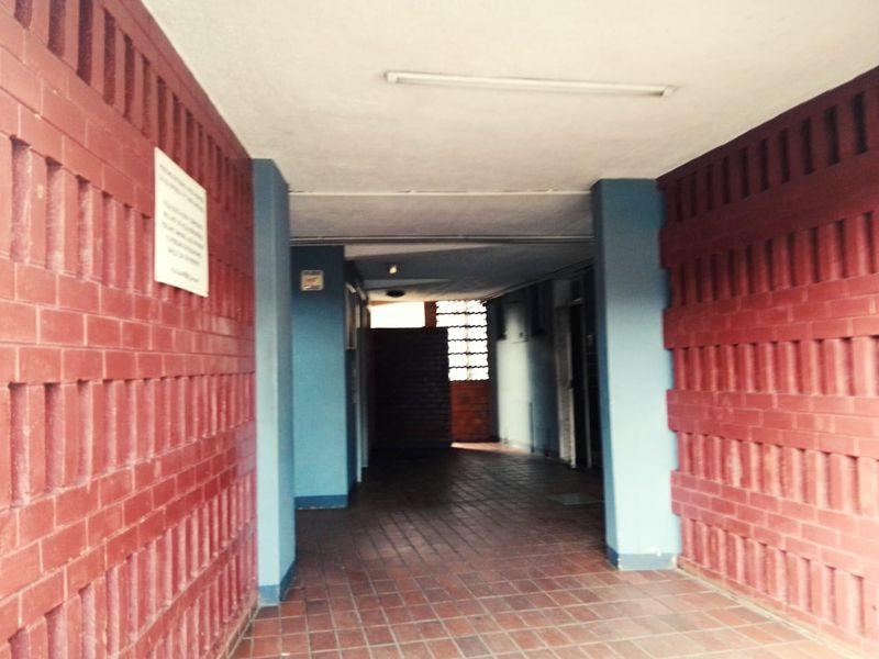 A covered apartment building hallway featuring red brick walls and tiled flooring, providing access to residential units.
