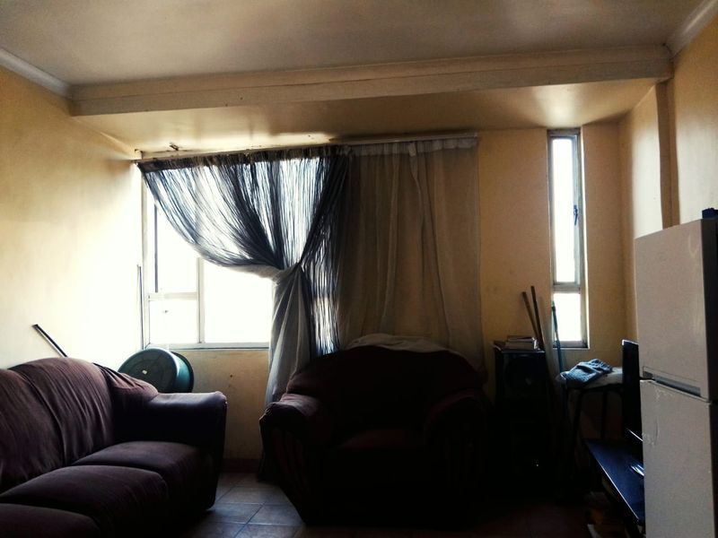 A living room area featuring tiled flooring and aluminium window frames, currently showing signs of wear and requiring cosmetic updates.