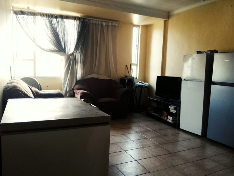 A living area featuring tiled flooring and large windows, currently in need of cosmetic updates to improve the overall aesthetic and brightness.
