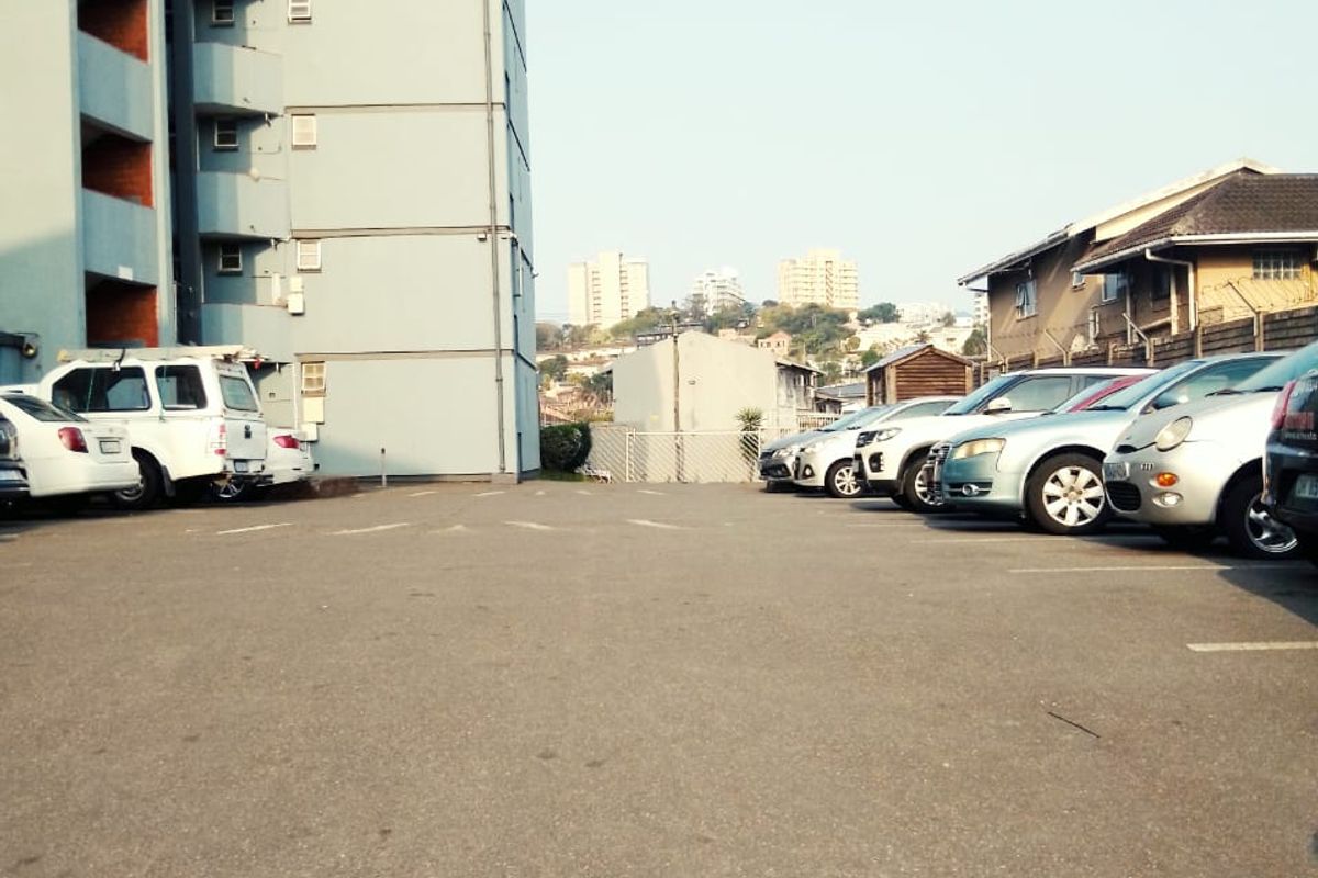 An outdoor parking area situated at the rear of a multi-story apartment building with paved bays and perimeter fencing.