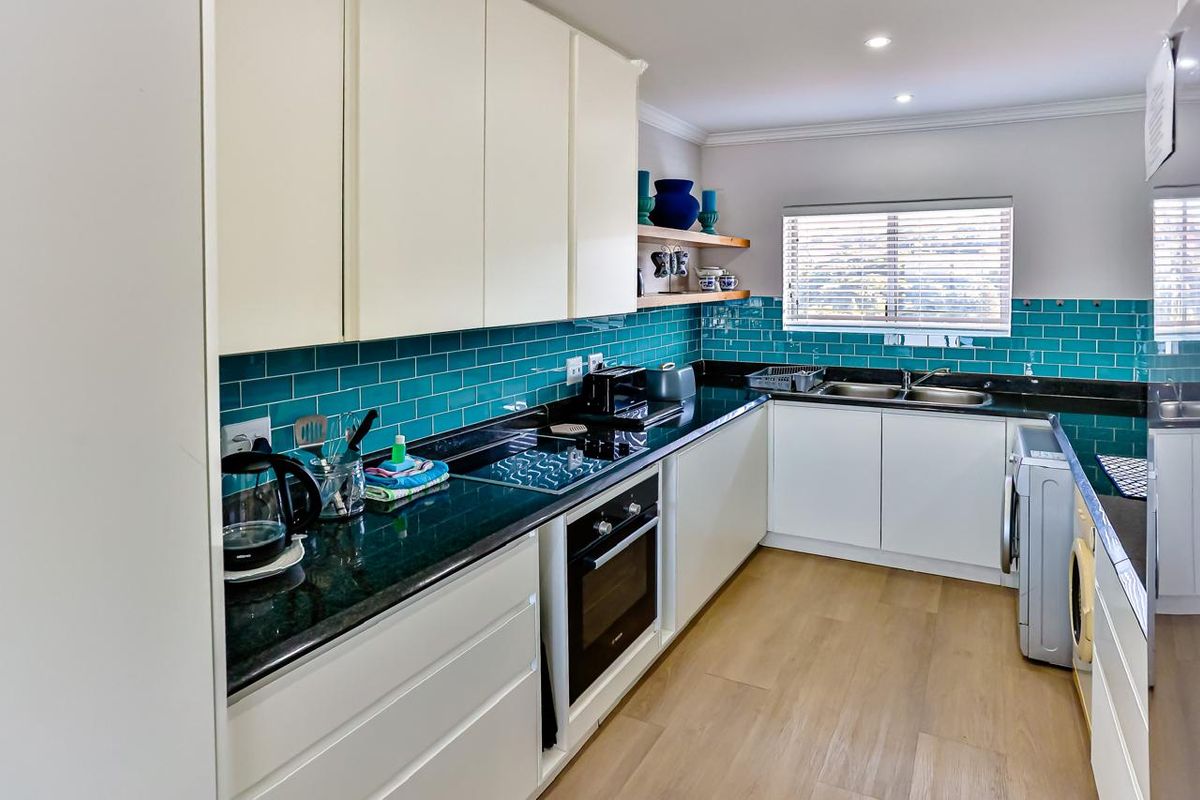 Modern kitchen featuring white cabinetry, dark granite countertops, vibrant teal subway tile backsplash, and integrated appliances with wood-look flooring.
