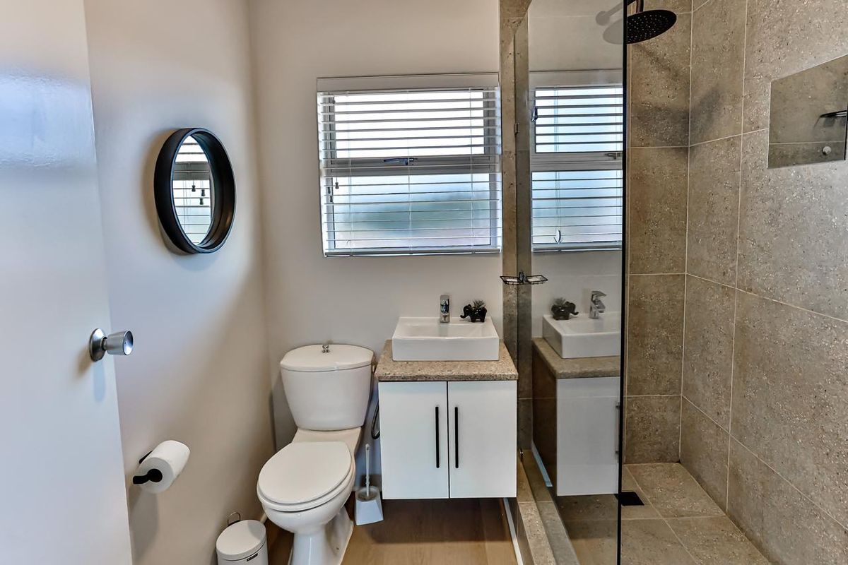 Modern bathroom featuring a vanity with basin, toilet, and a walk-in shower with tiled walls and glass screen.
