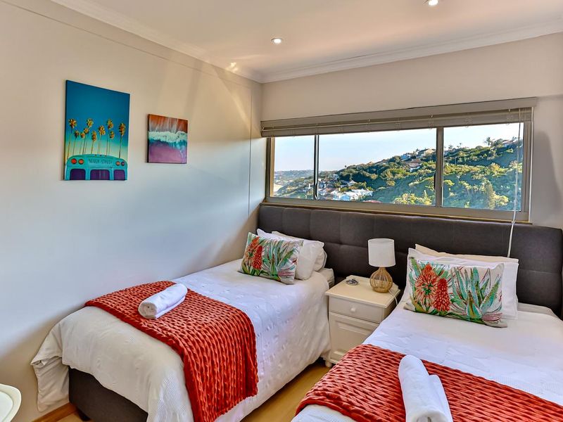 A well-maintained bedroom featuring laminate flooring, recessed downlights, and a large sliding window offering scenic hillside views.