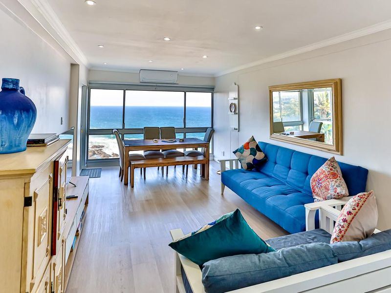 Bright open-plan living and dining area featuring laminate flooring, recessed lighting, and expansive ocean views through large sliding glass doors.