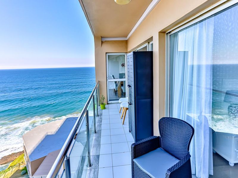 A spacious balcony featuring tiled flooring and a modern glass balustrade, offering stunning, unobstructed views of the ocean.