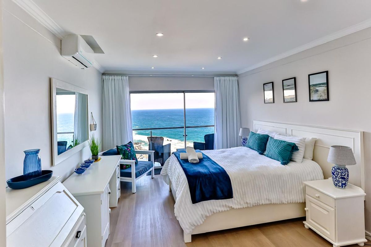 A well-maintained bedroom featuring laminate flooring, recessed lighting, air conditioning, and a sliding glass door opening to a scenic ocean view.