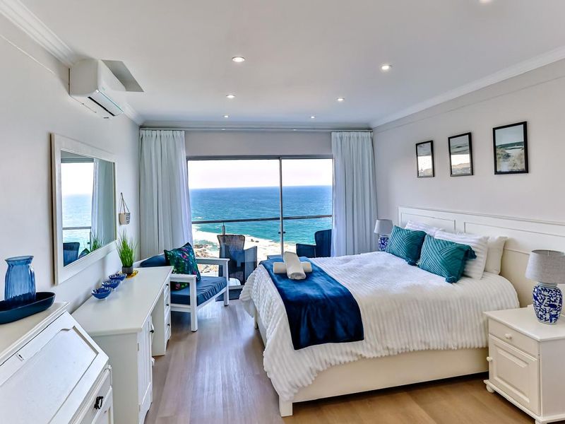 A well-maintained bedroom featuring laminate flooring, recessed lighting, air conditioning, and a sliding glass door opening to a scenic ocean view.