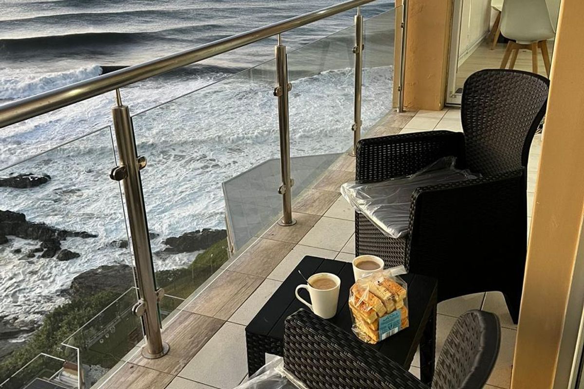 A balcony featuring a modern glass and stainless steel balustrade, tiled flooring, and direct ocean views.