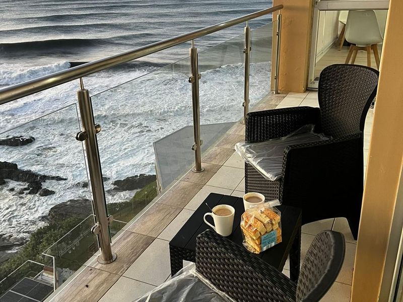 A balcony featuring a modern glass and stainless steel balustrade, tiled flooring, and direct ocean views.