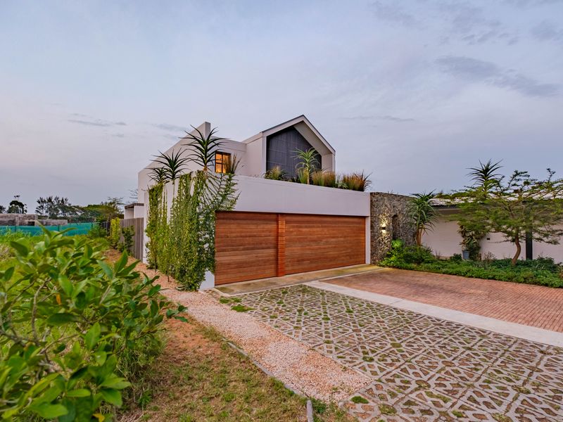 Modern architectural home featuring a double wooden garage door, stone facade accents, and a landscaped driveway with a rooftop terrace.