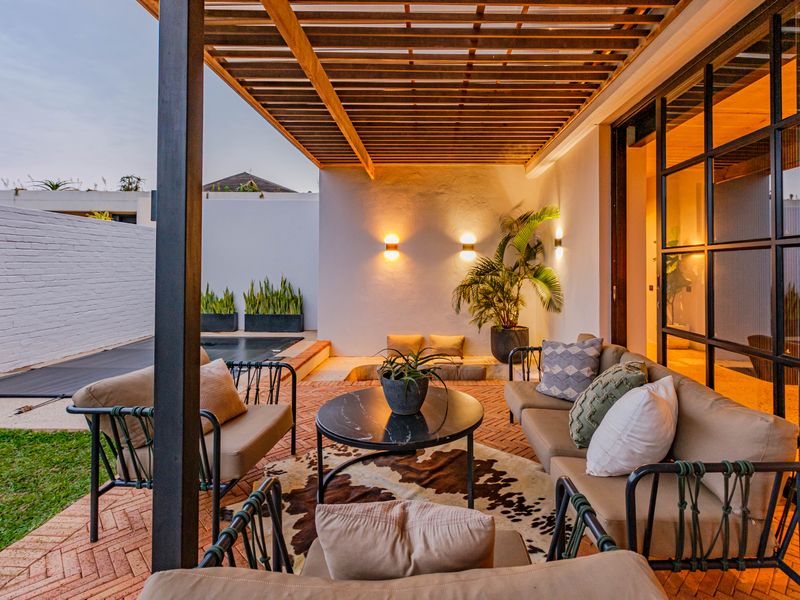 A beautifully designed covered patio featuring a timber pergola, brick flooring, and modern wall lighting, seamlessly connecting to the interior living space.
