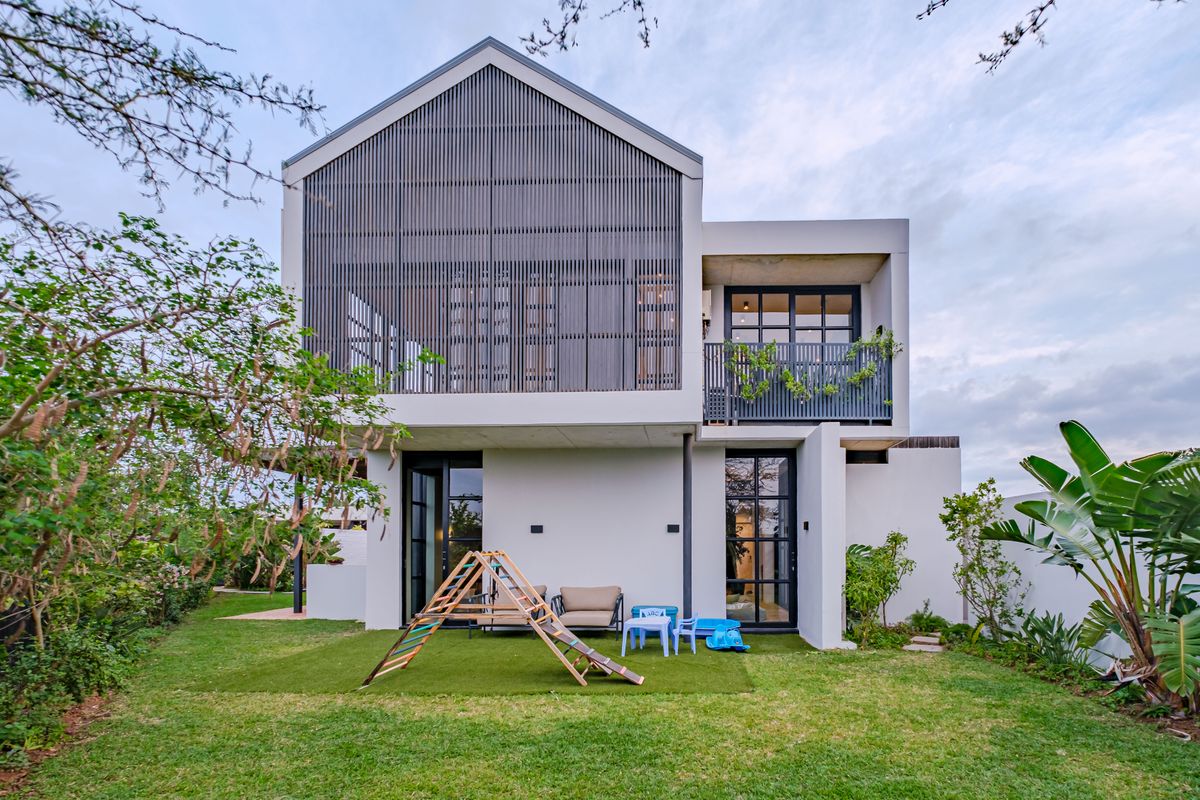 Modern two-story rear elevation featuring a timber slat screen, balcony, and large glass doors opening onto a landscaped garden with artificial lawn.