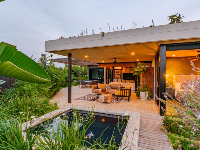 A modern covered patio featuring exposed aggregate flooring, recessed lighting, and seamless access to a plunge pool and landscaped garden area.