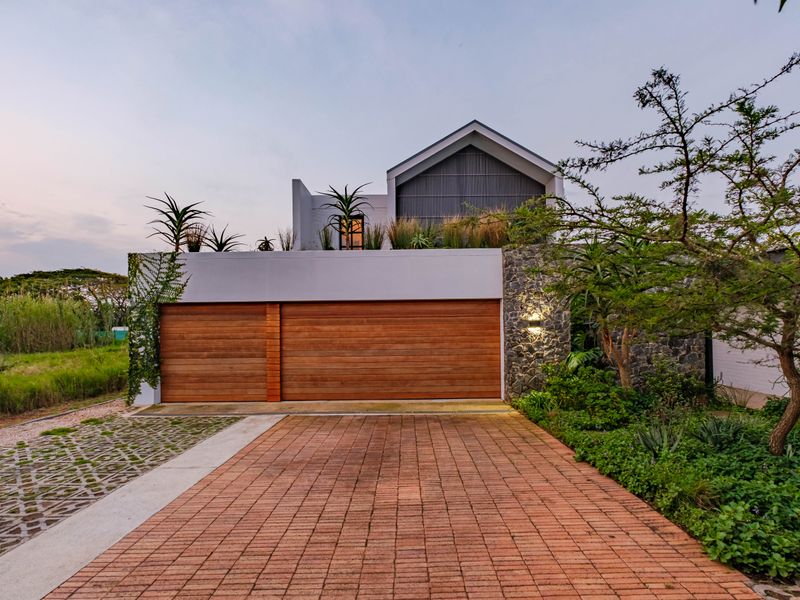 Modern architectural facade featuring a double garage with timber doors, stone cladding, and a landscaped roof garden, set against a paved driveway.