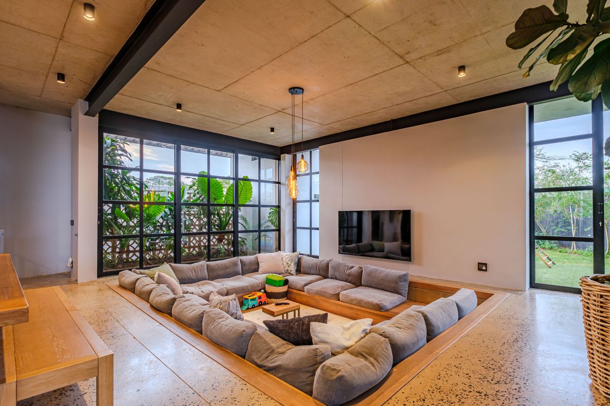 Modern living room featuring a unique sunken conversation pit, polished concrete floors, exposed concrete ceiling, and expansive steel-framed windows overlooking the garden.