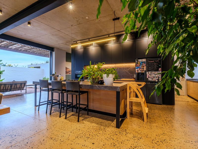 Modern open-plan kitchen featuring a large island with stone countertops, sleek cabinetry, and polished concrete floors, seamlessly connecting to an outdoor patio area.