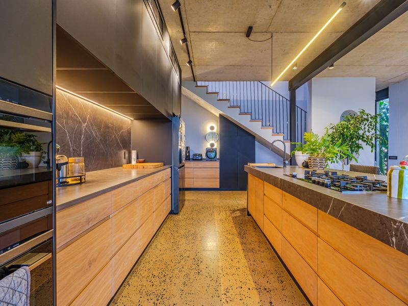 Modern kitchen featuring high-end cabinetry, stone countertops, a central island with gas cooktop, and an industrial-style exposed concrete ceiling.