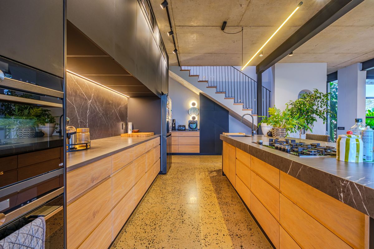 Modern kitchen featuring high-end cabinetry, stone countertops, a central island with gas cooktop, and an industrial-style exposed concrete ceiling.