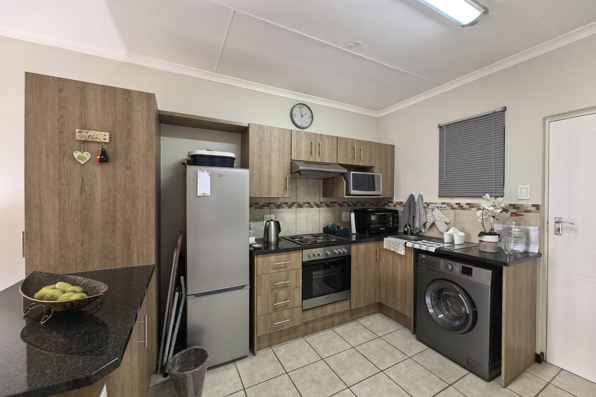 A functional kitchen featuring wood-look laminate cabinetry, granite countertops, a built-in oven with hob, and tiled flooring with integrated laundry space.