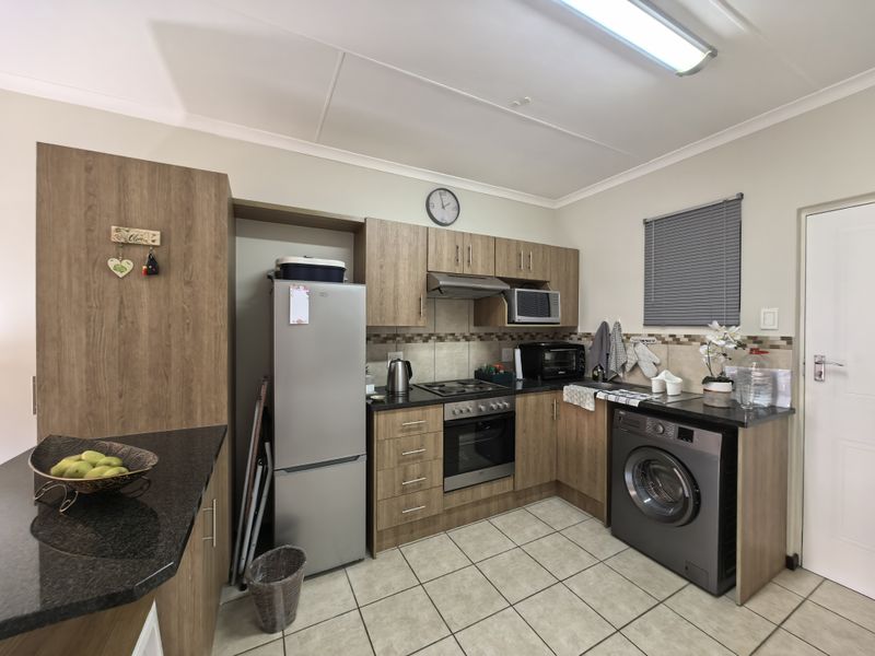 A functional kitchen featuring wood-look laminate cabinetry, granite countertops, a built-in oven with hob, and tiled flooring with integrated laundry space.