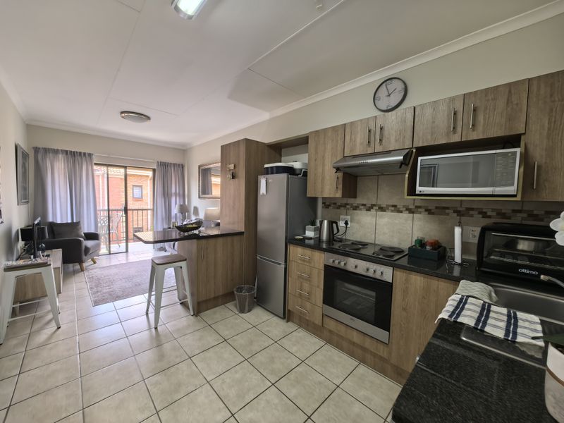 Open-plan kitchen and living area featuring wood-finish cabinetry, granite countertops, built-in appliances, and direct access to a balcony through sliding glass doors.