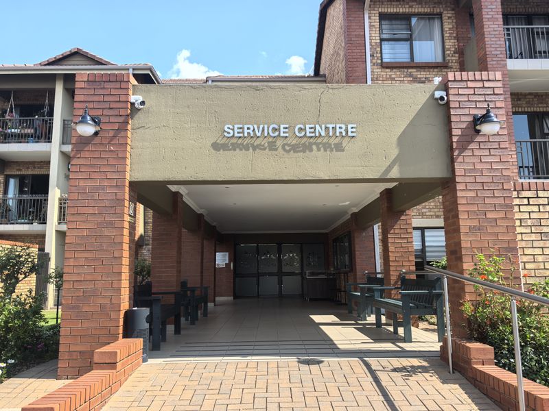 The entrance to the townhouse complex service centre features a covered brick portico, paved walkway, and exterior security lighting.
