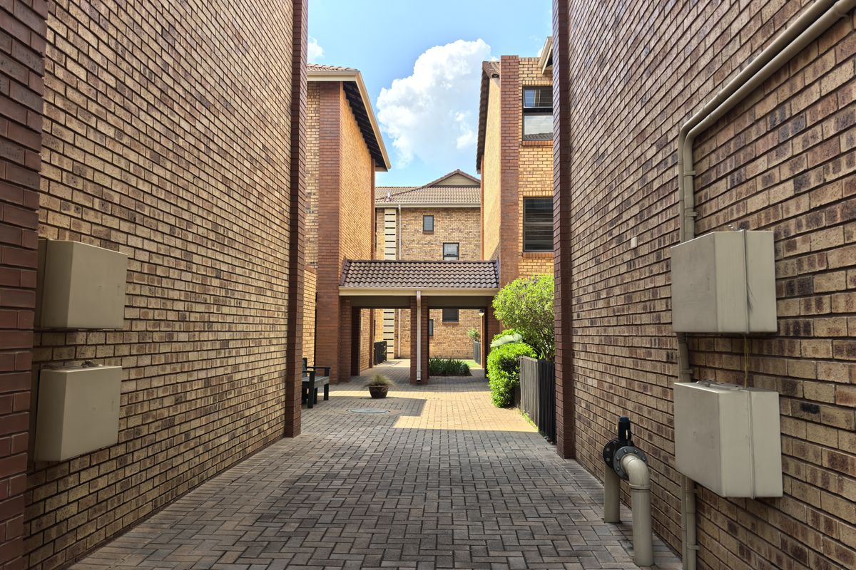 A paved walkway between townhouse blocks featuring exposed brick facades, utility infrastructure, and a covered transition area.