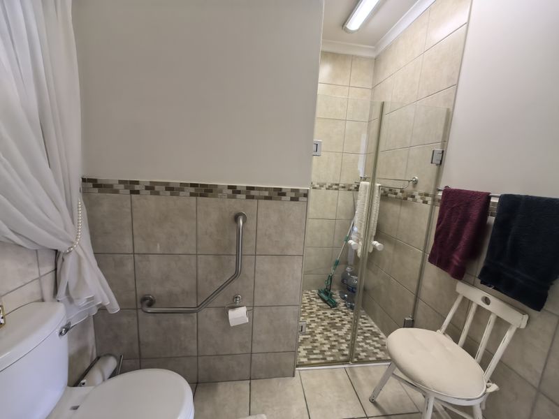 A functional bathroom featuring a walk-in shower with glass enclosure, grab rails for accessibility, and neutral tiled finishes with a decorative mosaic border.