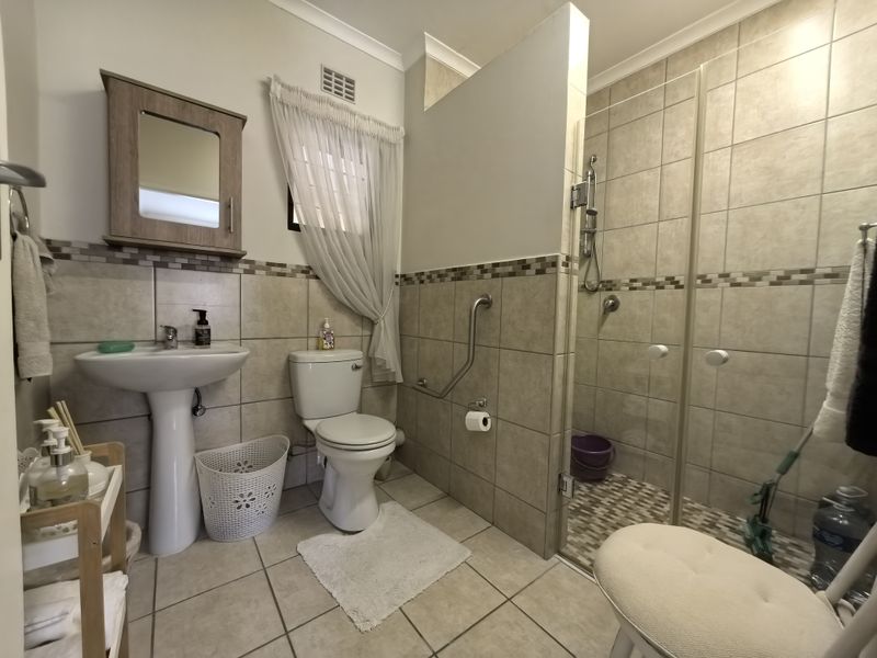A functional bathroom featuring a pedestal basin, toilet, and a walk-in shower with glass enclosure and safety grab rail.