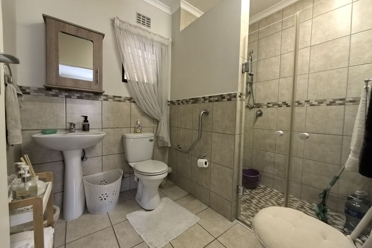 A functional bathroom featuring a pedestal basin, toilet, and a walk-in shower with glass enclosure and safety grab rail.