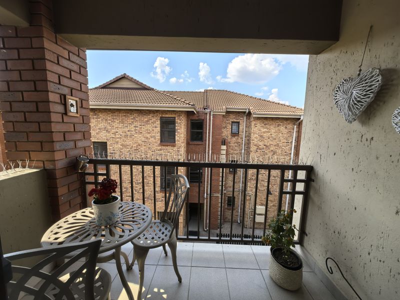 A covered balcony featuring tiled flooring, a brick pillar, and a metal balustrade with security spikes, overlooking the complex courtyard.