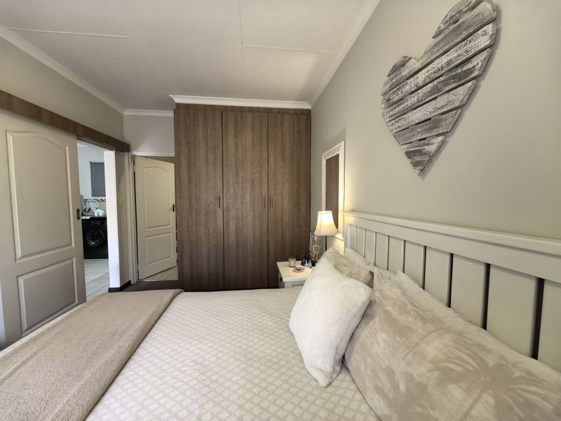A well-maintained bedroom featuring built-in wooden wardrobes, neutral wall finishes, and a sliding door providing access to an adjacent utility area.