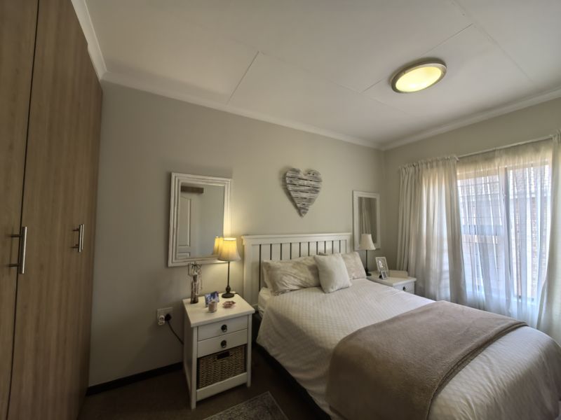 A cozy bedroom featuring a built-in wardrobe, neutral wall finishes, and natural light through window curtains.