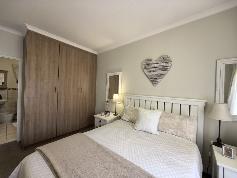 A well-maintained bedroom featuring a large built-in wardrobe with wood-grain finish and neutral wall tones, with an adjoining view into the bathroom.