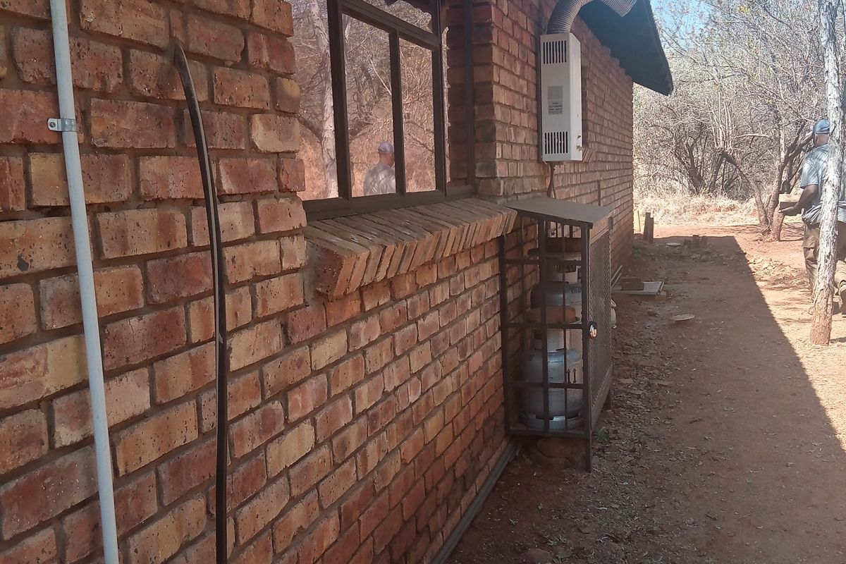 Rear exterior view of the house featuring exposed brick walls, a gas geyser installation, and a secure gas cylinder cage.