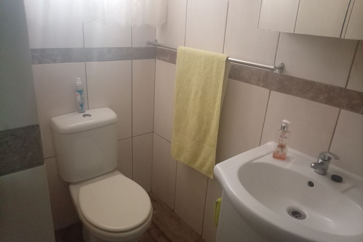 A compact bathroom featuring tiled walls, a standard toilet, a wall-mounted washbasin, and a medicine cabinet.
